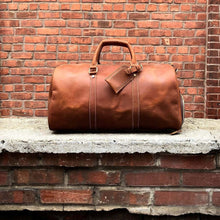 Load image into Gallery viewer, The Dagny Weekender | Large Leather Duffle Bag in full-grain leather on brick background, ideal for stylish and organized travel adventures.
