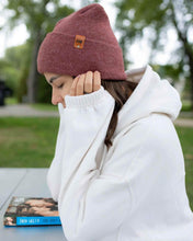 Charger l&#39;image dans la galerie, Person wearing NEW HAAKWEAR H-Stitch Cuffed Beanie in Rusty Burgundy while sitting outside with a book.
