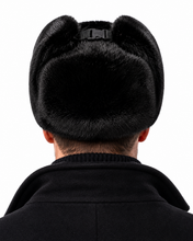 Load image into Gallery viewer, Rear view of a person wearing a black fur ushanka hat with ear flaps and a black collar coat, isolated on a white background.
