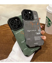 Load image into Gallery viewer, Two Luxury Leather Sneaker Phone Cases with sleek design and suede labels held over a wooden table next to a Starbucks cup.
