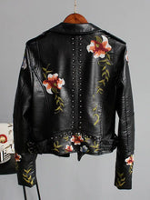 Cargar imagen en el visor de la galería, Floral Print Faux Leather Jacket with bold floral design and edgy punk rock elements, showcasing unique style on a hanging display.
