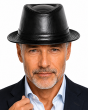 Load image into Gallery viewer, A close-up portrait of a man wearing a black leather fedora hat, a light blue dress shirt, and a dark suit jacket against a plain white background.
