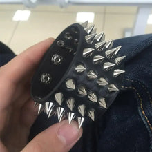 Load image into Gallery viewer, Faux leather bracelet with spikes showcasing punk-inspired style, held by a hand above a denim background. Ideal for edgy fashion.
