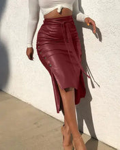 Load image into Gallery viewer, Woman wearing a burgundy high-waist faux leather midi skirt with belt and button trim, paired with a white crop top.
