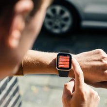 Load image into Gallery viewer, Person interacts with an Apple Watch 5 displaying a red screen, wearing a stylish watch band in an outdoor setting.
