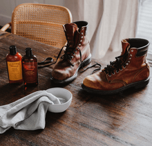 Load image into Gallery viewer, Leather Cleaner with boots on wooden table, showcasing gentle, non-toxic formula effective on leather, vinyl, and faux leather surfaces.
