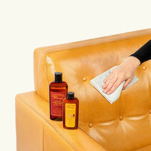 Cargar imagen en el visor de la galería, Person using Lint-Free Application Cloth with Leather Honey products on a tan leather couch for smooth, debris-free application.
