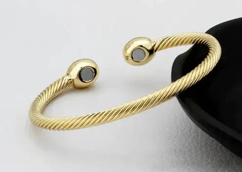 Elegant gold magnetic bracelet on a textured surface, showcasing its chic design and healing properties for modern style enthusiasts