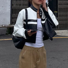 Charger l&#39;image dans la galerie, Woman wearing a stylish patchwork vegan leather jacket with bold black and white design, holding a phone, street scene background.
