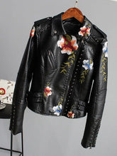 Cargar imagen en el visor de la galería, Floral print faux leather jacket with edgy punk style and romantic floral designs, hung on a wooden hanger.
