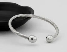 Load image into Gallery viewer, Silver magnetic bracelet with a twisted design and polished ends, suitable for therapy and style, placed on a stylish black surface.
