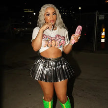 Cargar imagen en el visor de la galería, Woman in metallic pleated mini skirt and graphic tee holding a pink fan at night.
