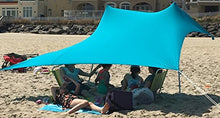 Load image into Gallery viewer, People relaxing under the eZthings UV Sun Shade Beach Shelter with sandbag anchors on a sunny beach.
