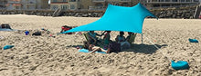 Load image into Gallery viewer, Beachgoers enjoying shade under a bright blue eZthings UV sunshade with sandbag anchors.

