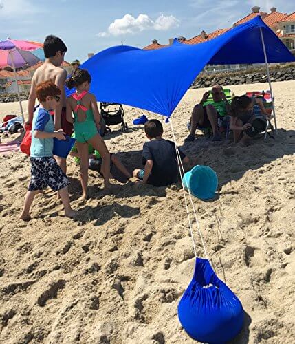 Royal Blue UV Light Sun Shade Protection Beach Shelter with Sandbag Anchors providing sunburn protection on a sunny beach day.