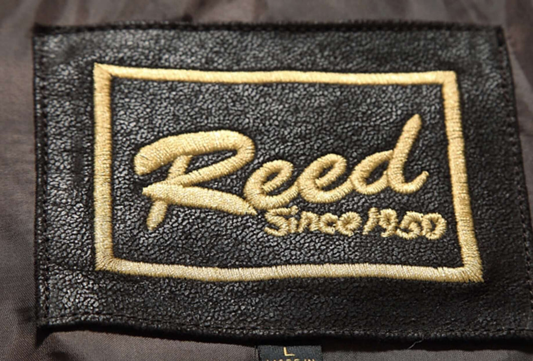 A close-up of a black leather gift card with the brand name 'REED' written in gold letters, indicating the material and branding since 1950.